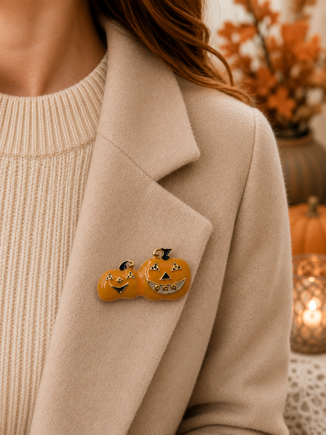 A close-up of a person wearing a beige coat over a cream ribbed sweater, with a small orange jack-o'-lantern pin on the lapel. The background is softly blurred with autumn decor.