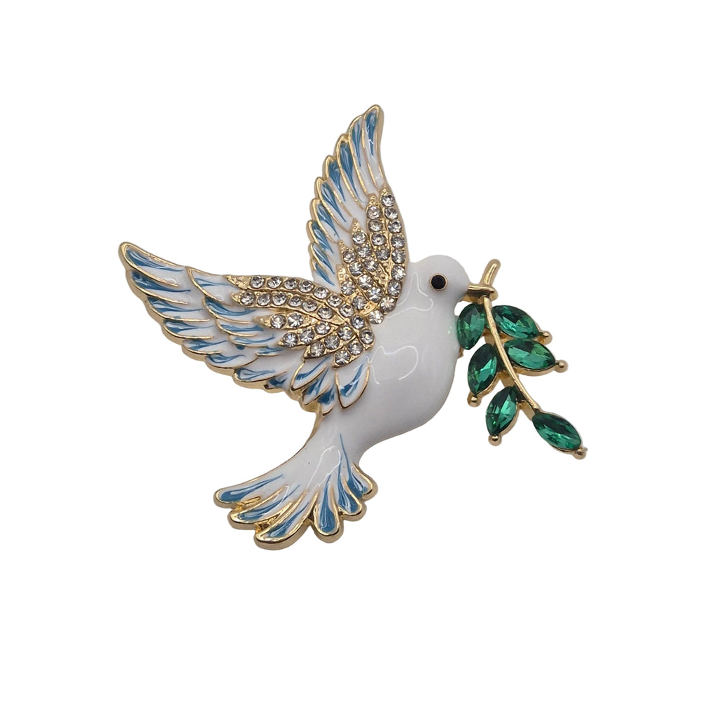 A white enamel dove brooch with gold-plated trim, blue enamel wing details, rhinestone embellishments on the wings, and a green leafy branch in its beak, shown on a plain white background.