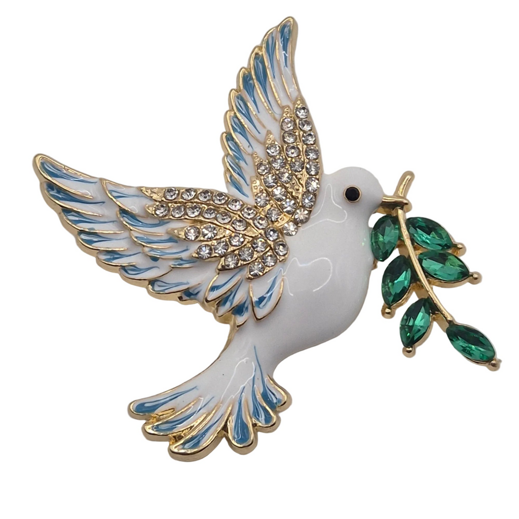 A white enamel dove brooch with gold-tone metal outlines, blue enamel accents on the wings, clear rhinestones across the body, and a green crystal-embellished olive branch in its beak, shown on a plain white background.
