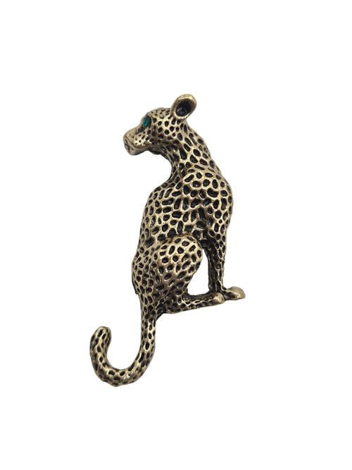 A leopard-shaped brooch or pin with a spotted pattern, featuring a small green stone for an eye, set against a plain light gray background.