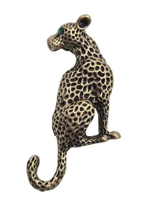 A leopard-shaped brooch or pin in an antique gold finish with blackened spots and a small green eye detail, shown on a plain white background.