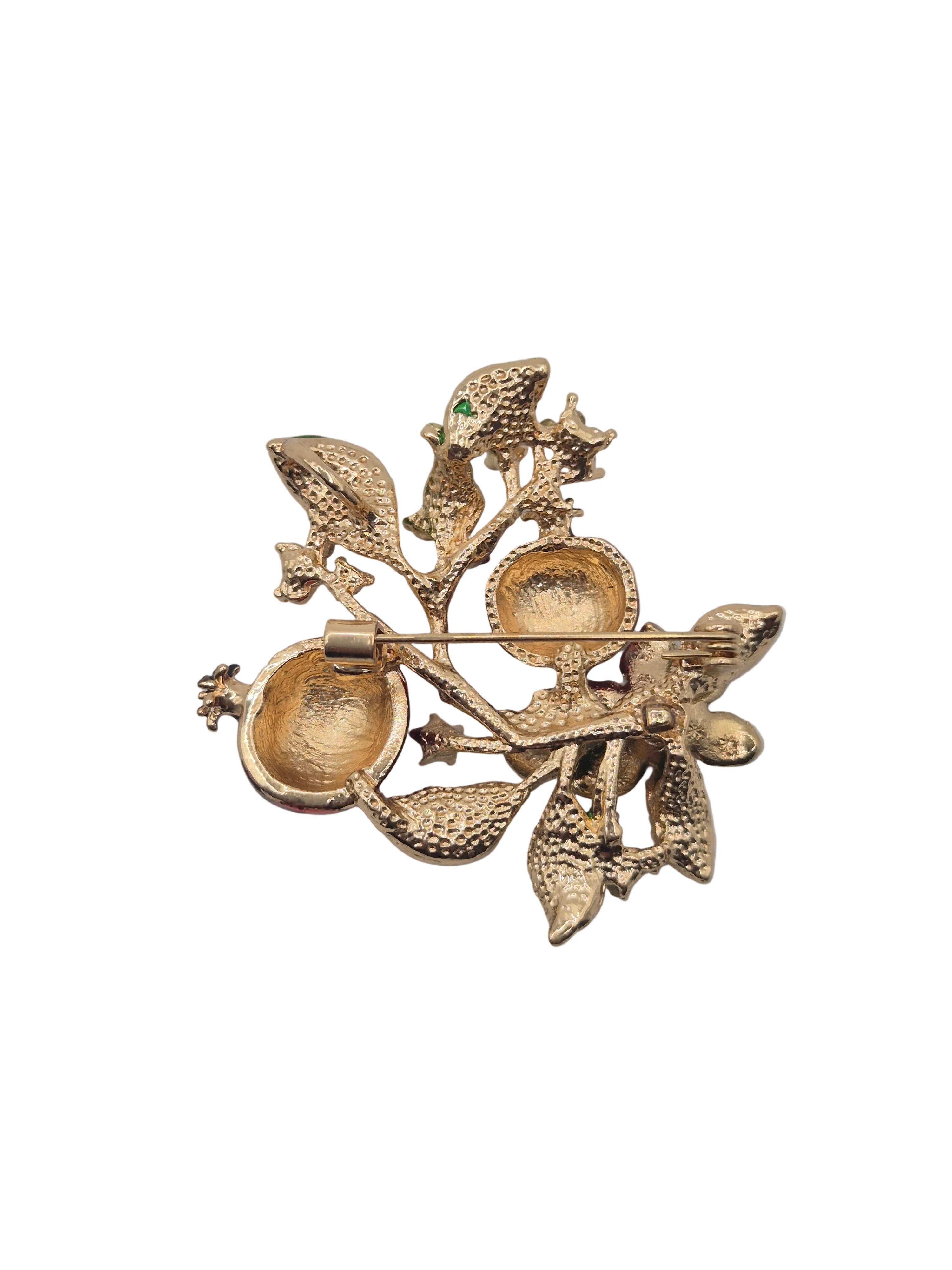 A vintage gold-tone brooch featuring a stylized branch with textured leaves, small berries, and a tiny green stone accent, photographed on a plain white background.