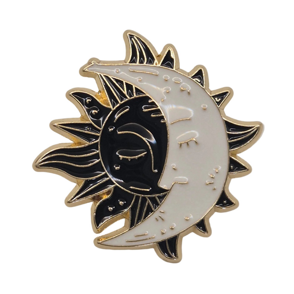 A crescent moon and sun enamel pin with a black and white design, featuring a crescent moon face, sun rays, and small stars, outlined in gold-tone metal on a plain white background.