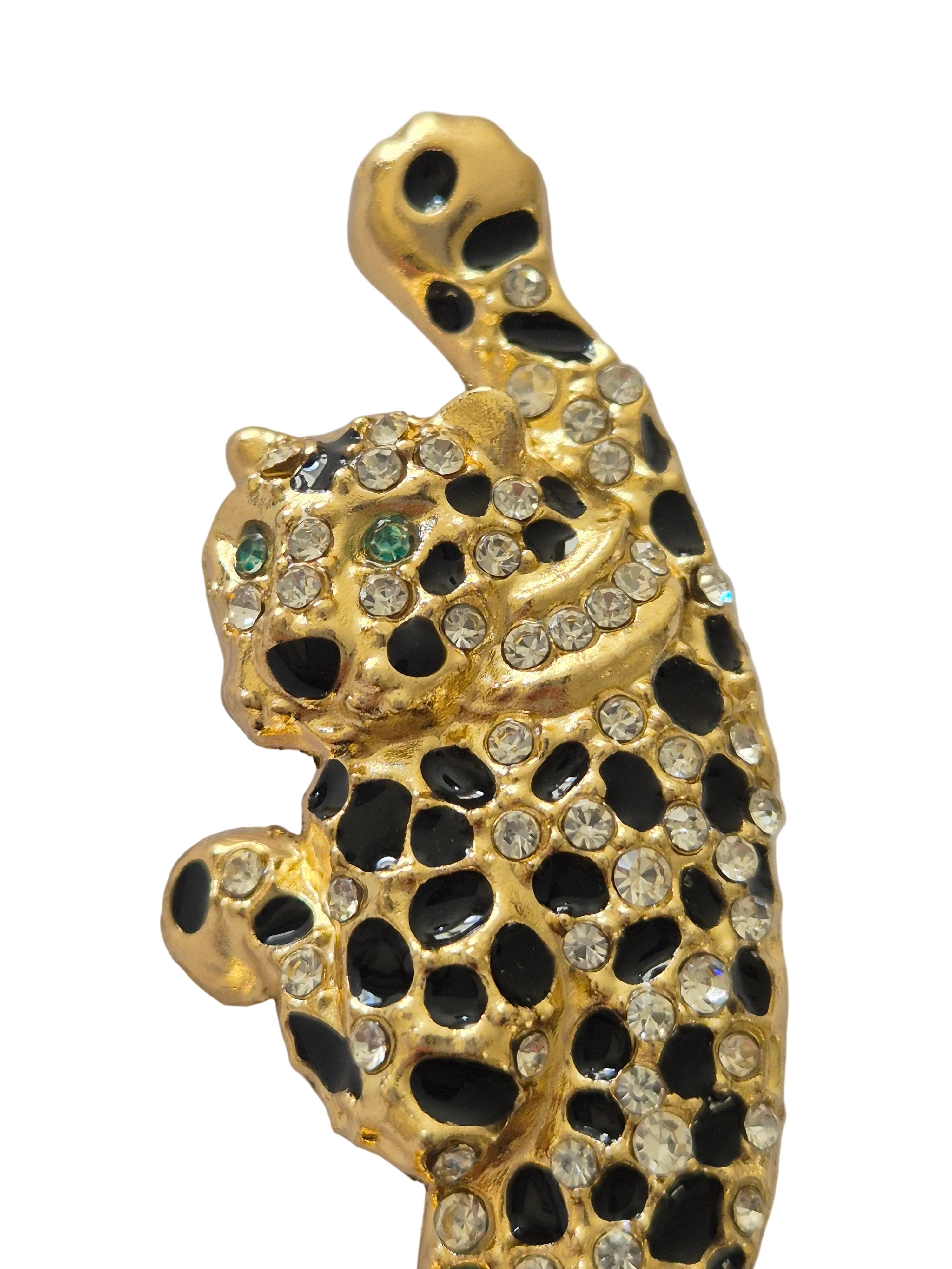 Gold leopard brooch with black and green gemstones on a light gray background