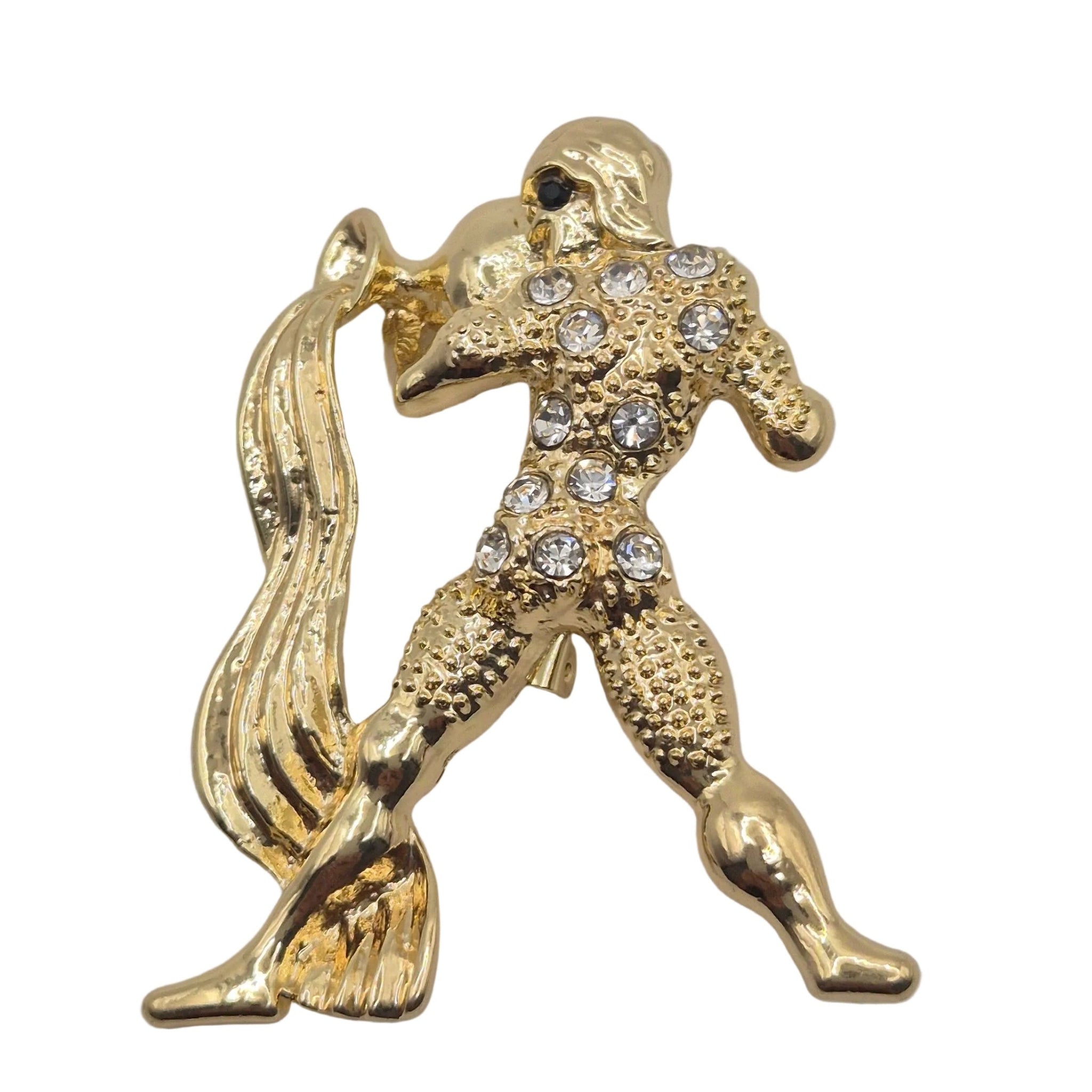 A gold-tone metal Aquarius brooch depicting a stylized figure adorned with clear rhinestones, shown on a plain white background.
