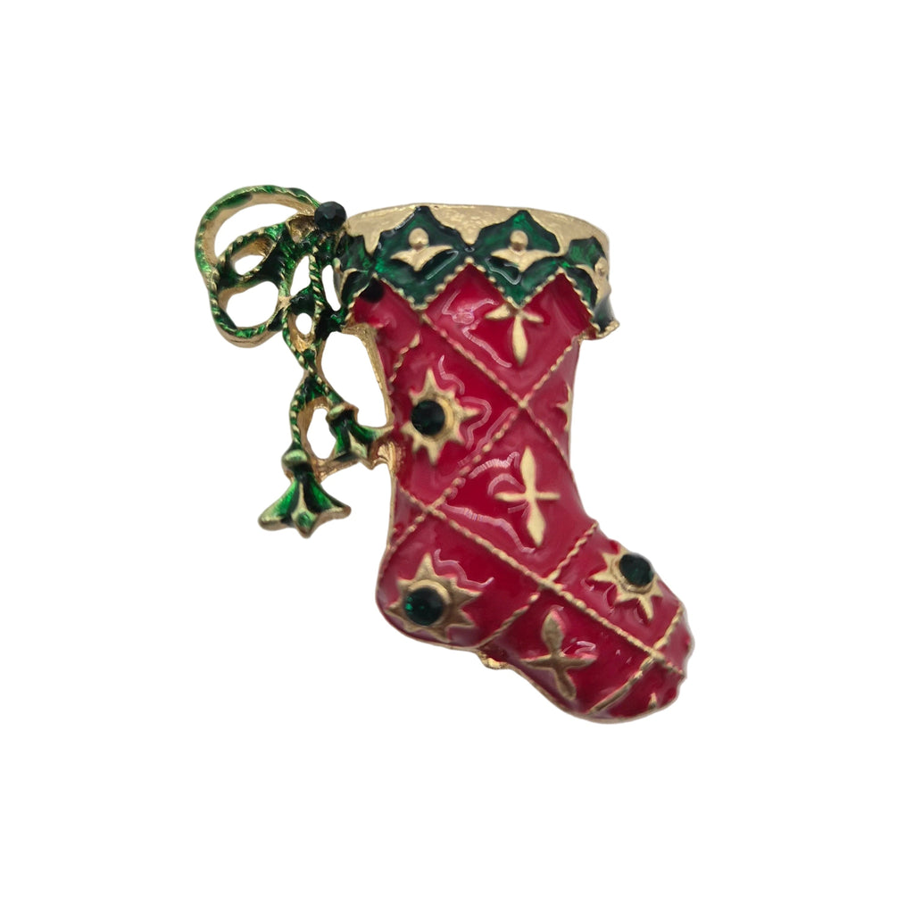 A Christmas stocking brooch with a red enamel body, gold-tone metal trim, green holly accents, and small black rhinestone details, shown on a plain white background.