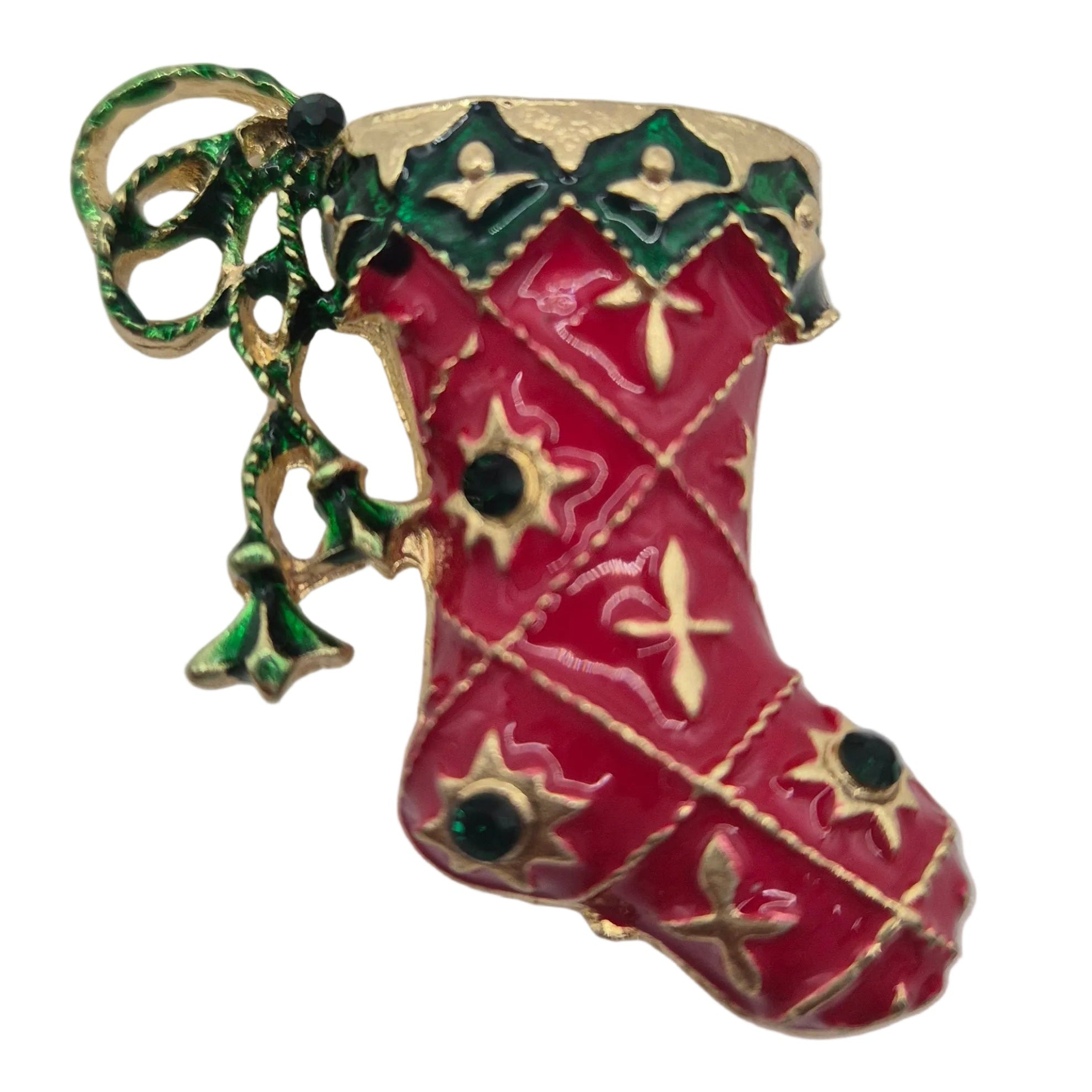 A Christmas stocking brooch featuring red enamel, gold-tone metal detailing, green holly accents, and small black stone embellishments, shown on a plain white background.