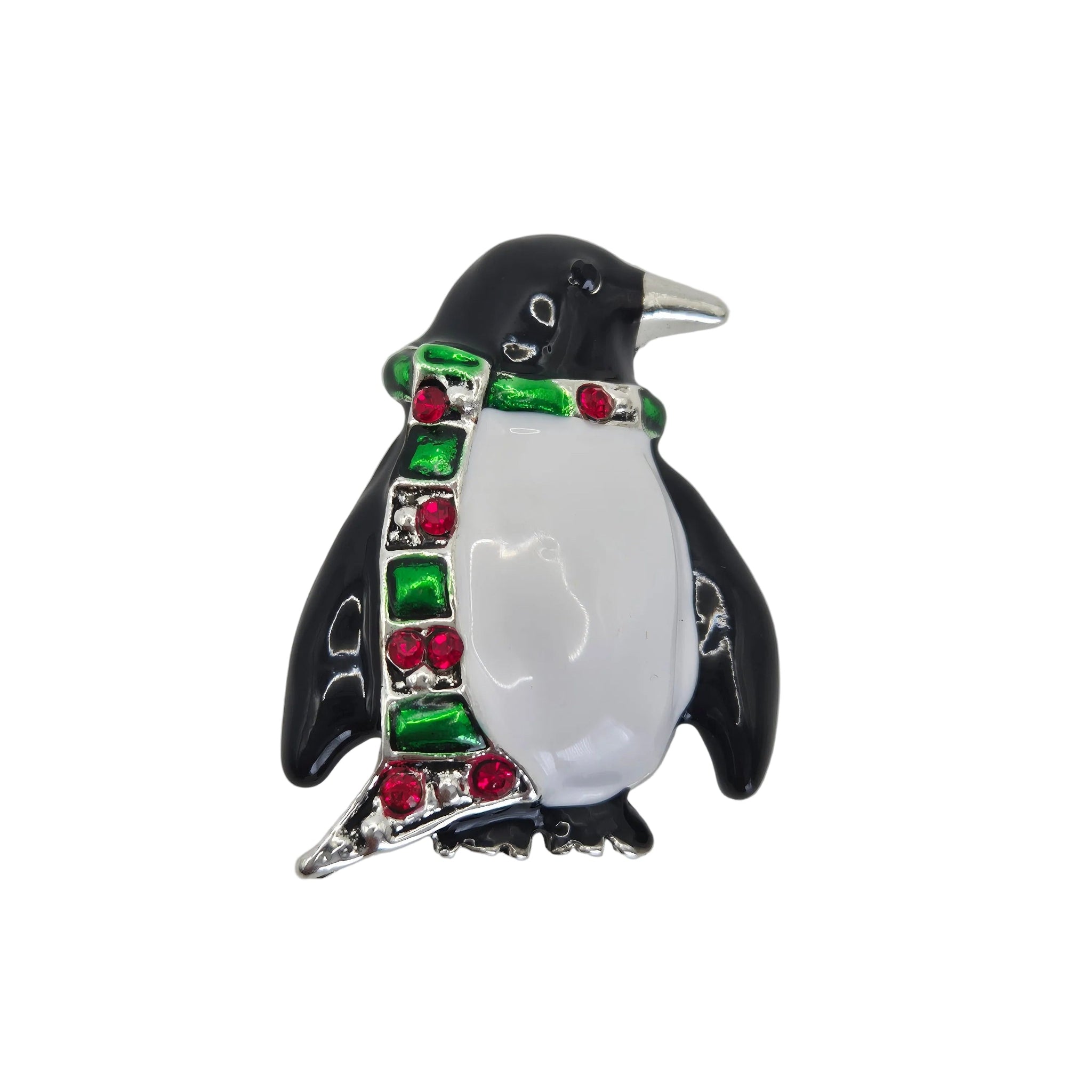 A penguin-shaped brooch with a glossy black and white enamel body, wearing a green and red rhinestone scarf, set against a plain white background.
