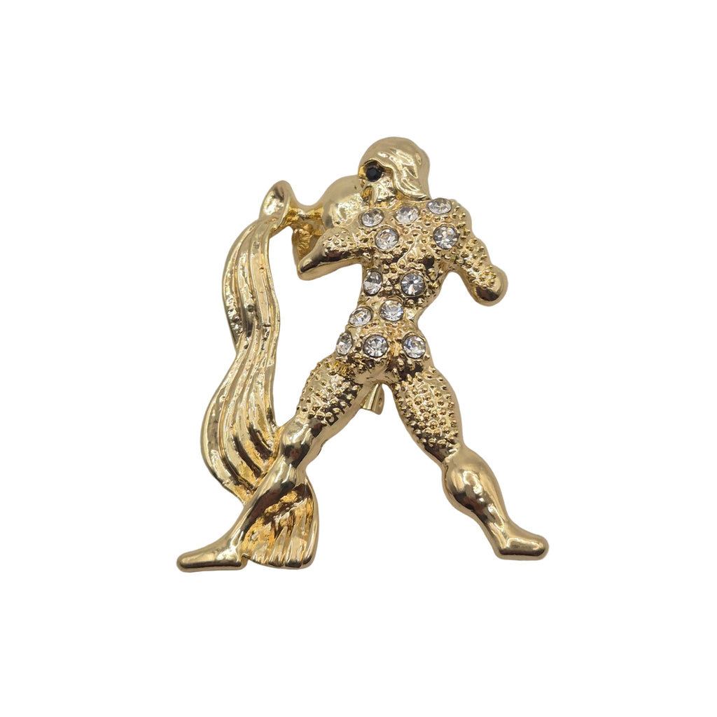 A gold tone metal Aquarius zodiac sign brooch with rhinestone detailing. Displayed against a plain white background.