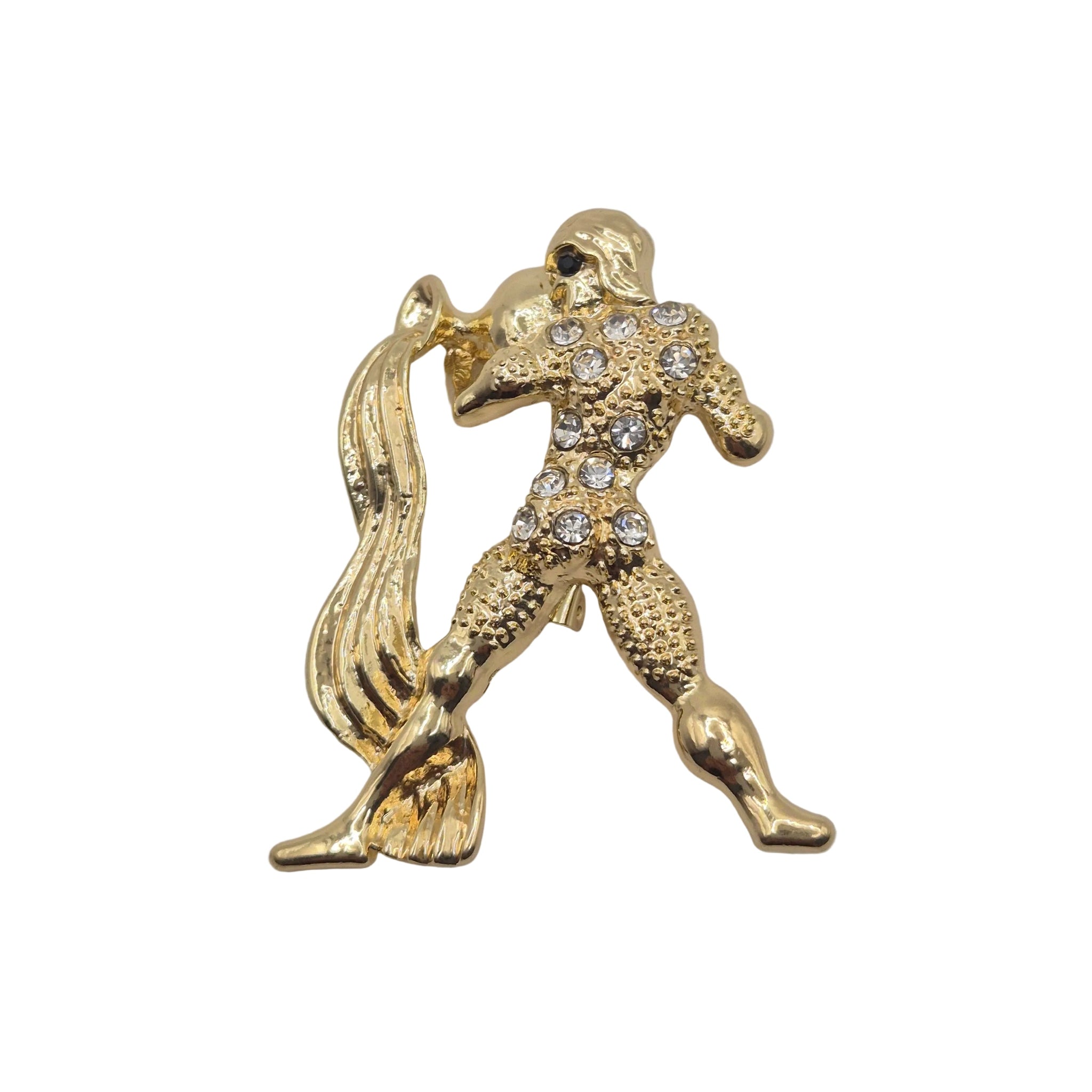 A gold tone metal Aquarius zodiac sign brooch with rhinestone detailing. Displayed against a plain white background.