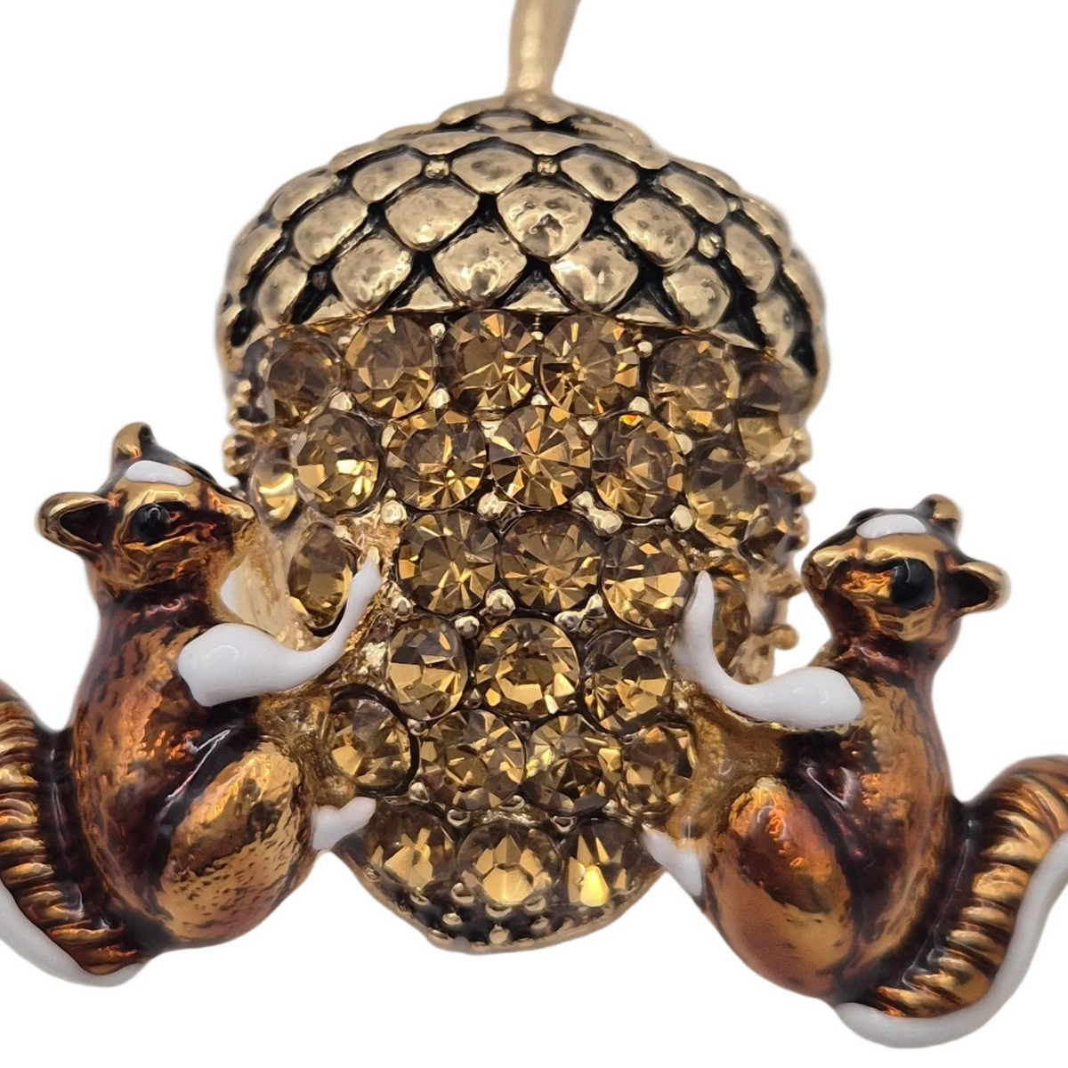 A close up shot of a vintage-style gold tone brooch or pendant featuring two small squirrels flanking a large acorn embellished with rhinestones, set against a plain white background.