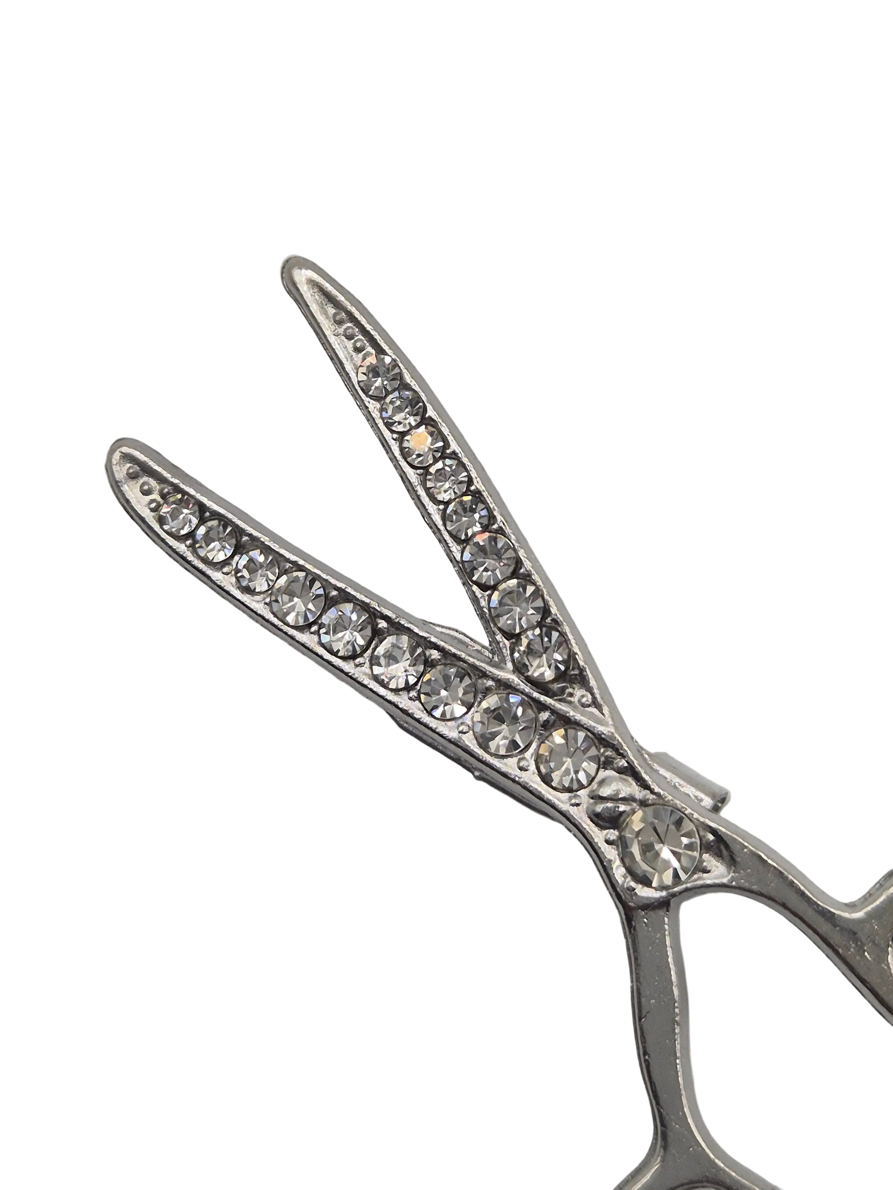 Silver scissors-shaped brooch with crystal embellishments on a white background