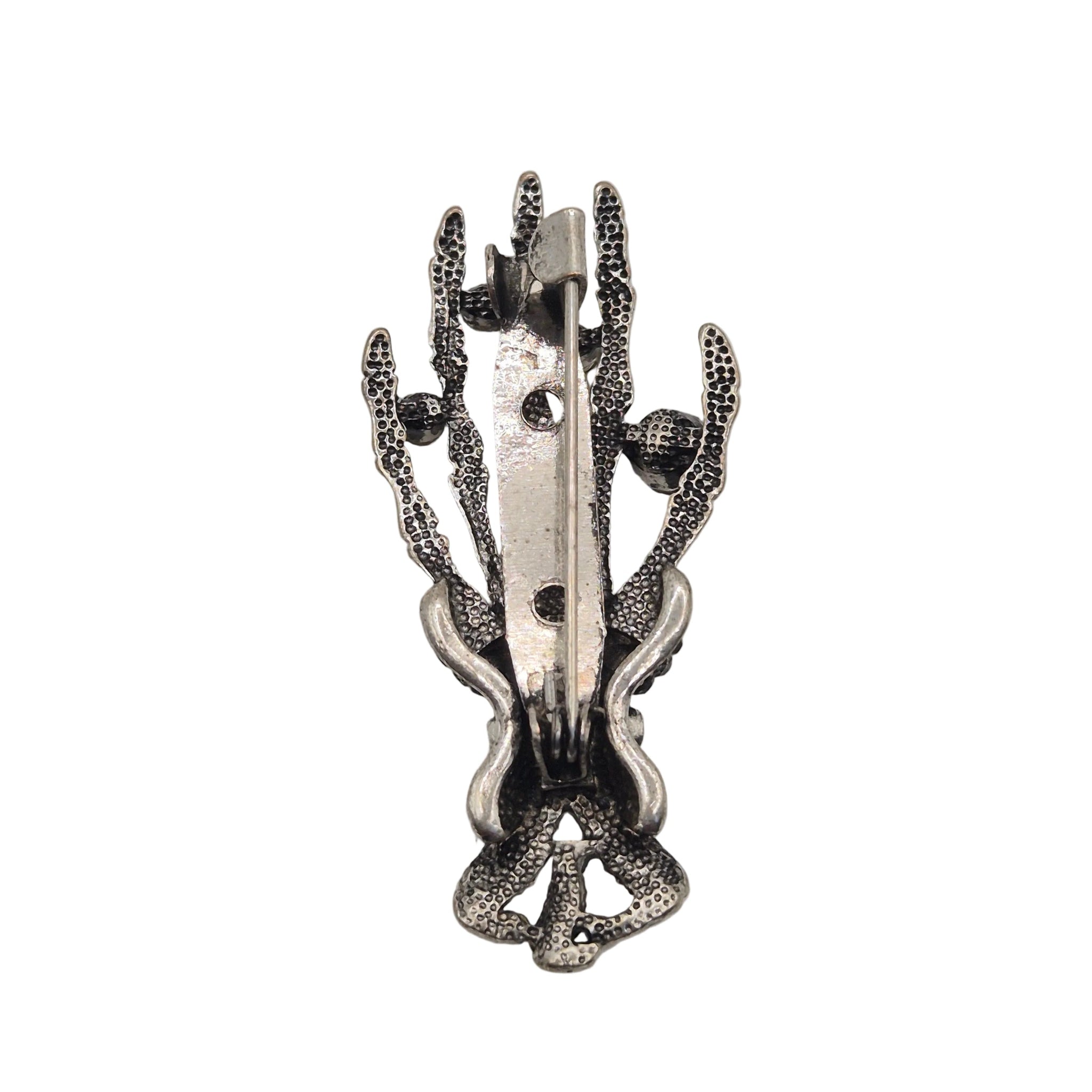 A silver-toned metal pin shaped like a skeleton hand, showing reverse side against a plain white background.