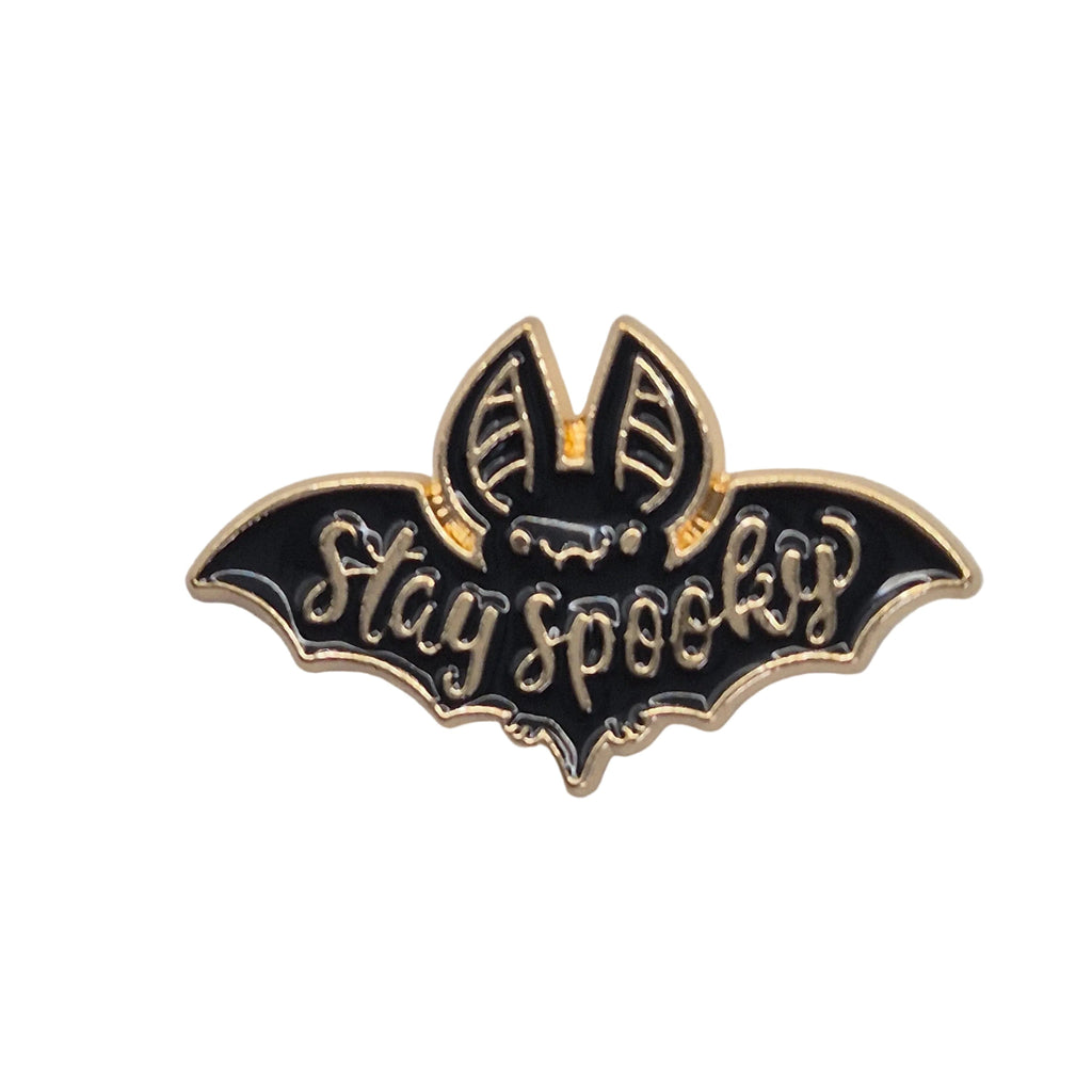 A black and gold enamel lapel pin shaped like a bat with the words 'Stay spooky' written across it, shown on a plain white background.