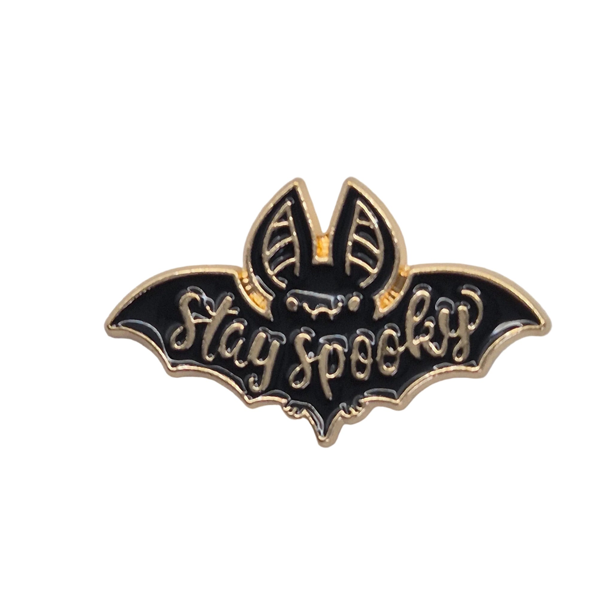 A black and gold enamel lapel pin shaped like a bat with the words 'Stay spooky' written across it, shown on a plain white background.