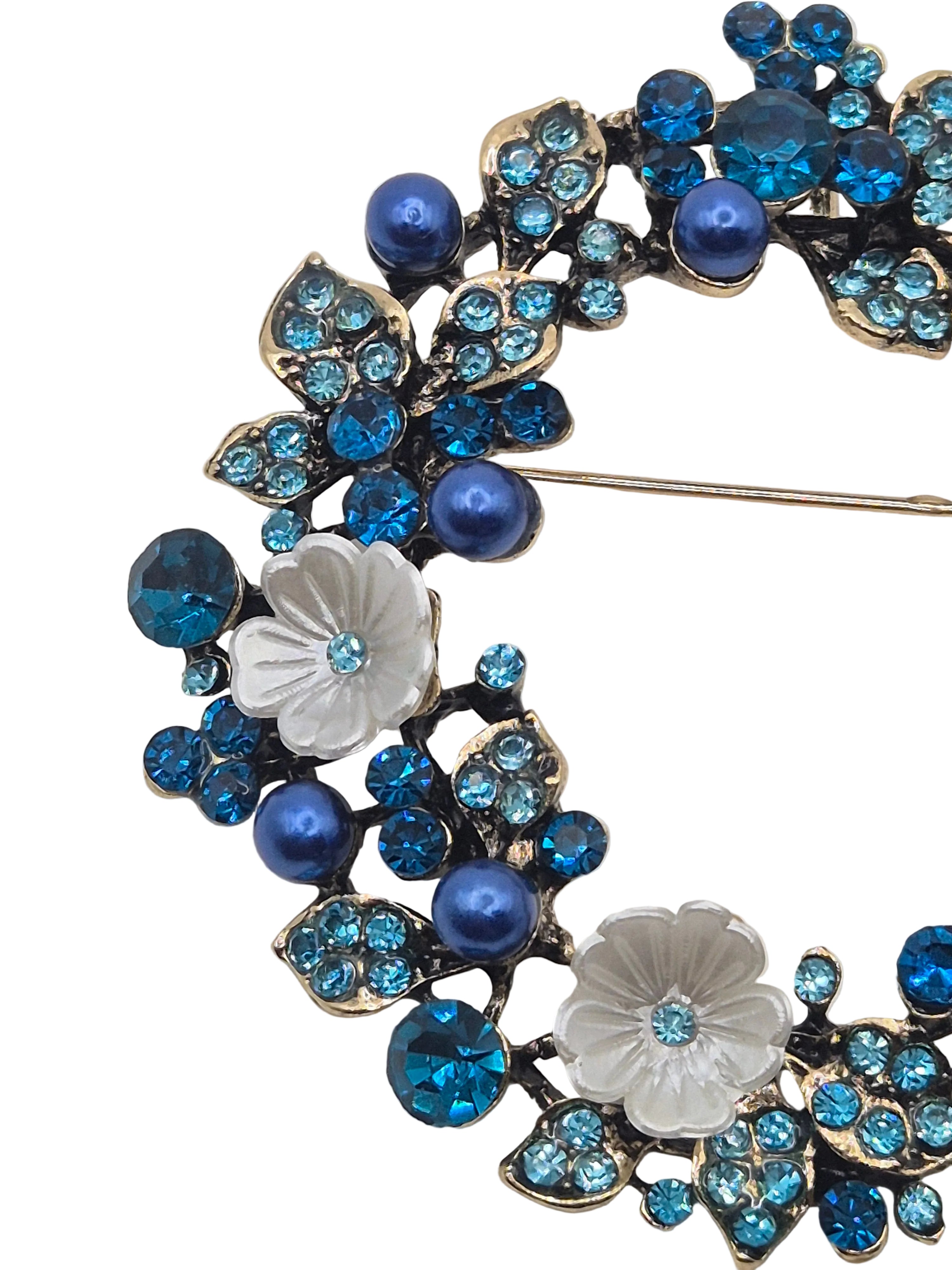 Decorative brooch with blue gemstones and white floral design on a light gray background