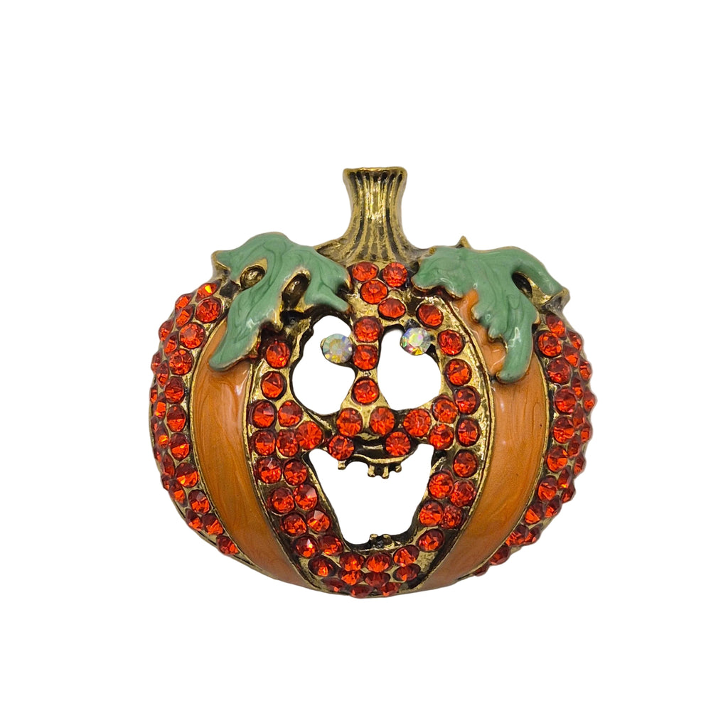 A vintage pumpkin-shaped brooch featuring a gold-tone metal base, decorated with rows of orange-red rhinestones and two light green enamel leaves on a plain light gray background.
