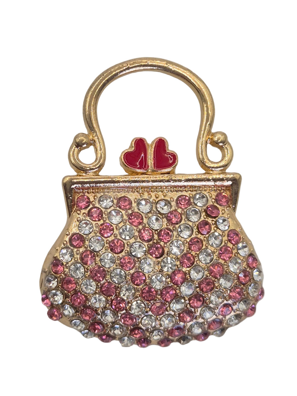 A gold-tone purse-shaped brooch embellished with pink and clear rhinestones, featuring a small red heart detail on the handle, set against a plain white background. Close up view.