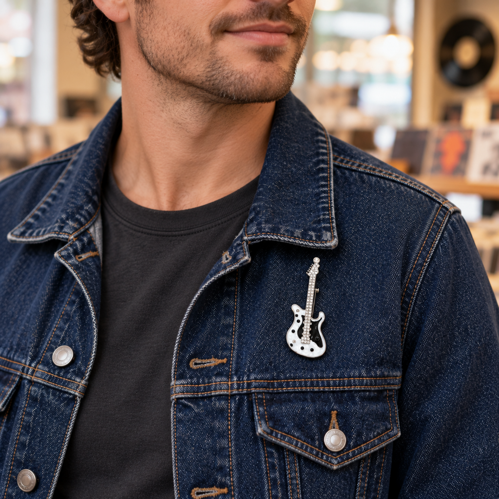 A close-up of a man wearing a dark blue denim jacket over a black t-shirt, featuring a silver guitar-shaped lapel pin on the chest pocket.