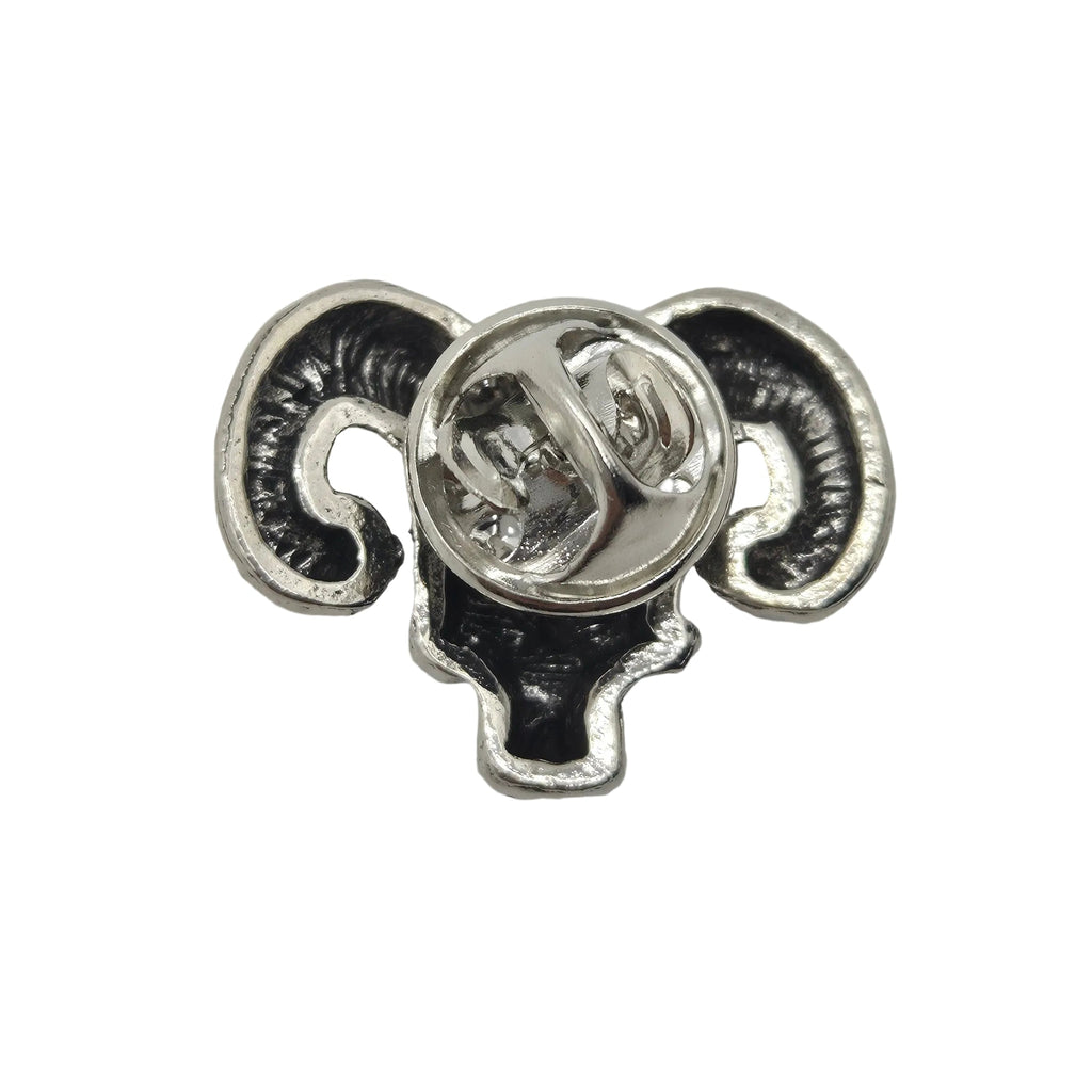 A close-up of the back of a small metal pin or badge shaped like a ram's head, with curved black enamel horns and a silver-tone clasp on a plain white background.