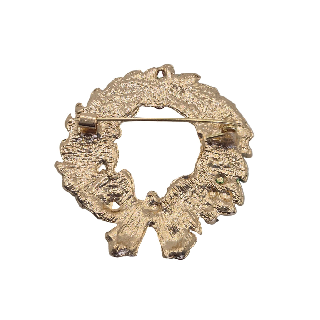 A textured gold-tone metal brooch shaped like a stylized bow or floral wreath, photographed on a plain light gray background.