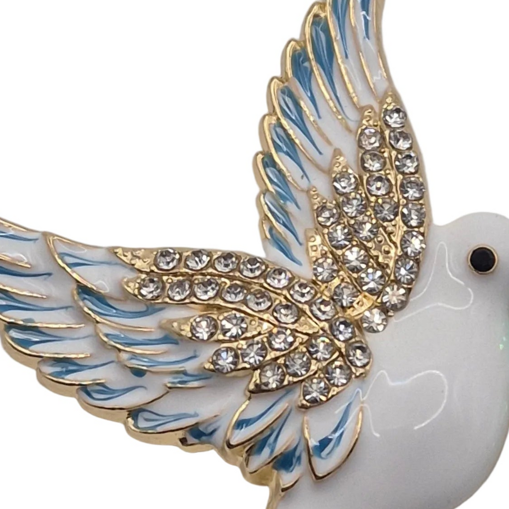 A close-up of a white dove brooch with gold-plated outlines, light blue enamel feather details, and clear rhinestones on the wing, shown against a plain white background.
