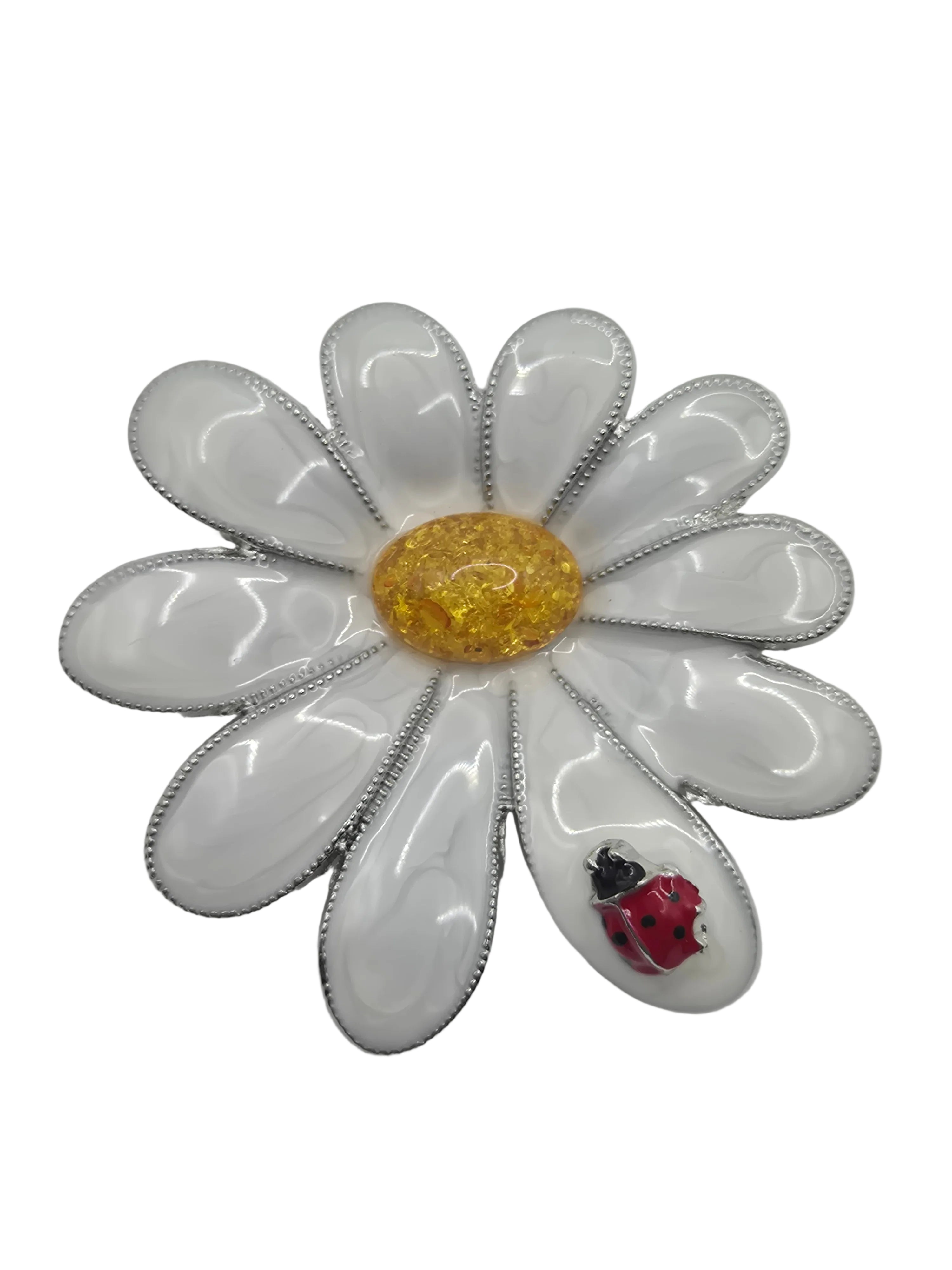 Floral daisy brooch with white petals, yellow center, and red ladybug on a gray background