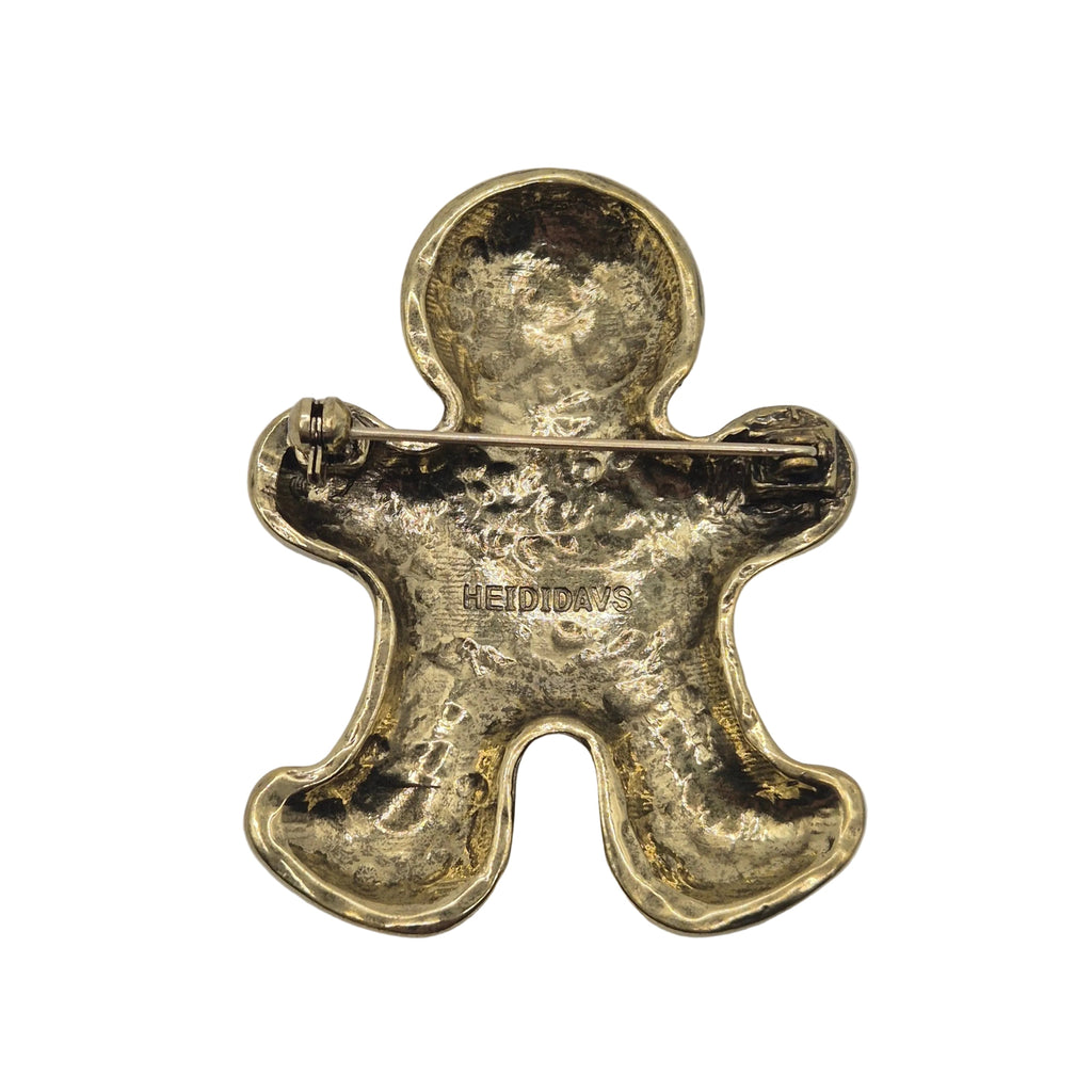 A gold-toned gingerbread man brooch shown from the back, displaying its hammered texture and a safety pin clasp on a plain white background.