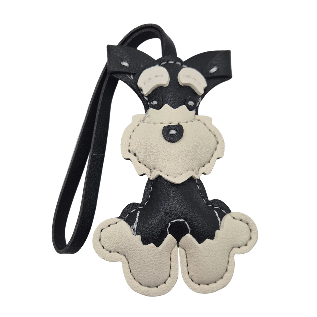 A small dog-shaped leather keychain or bag charm with a black body, cream-colored snout, ears, and paws, attached to a black strap, shown on a plain white background.