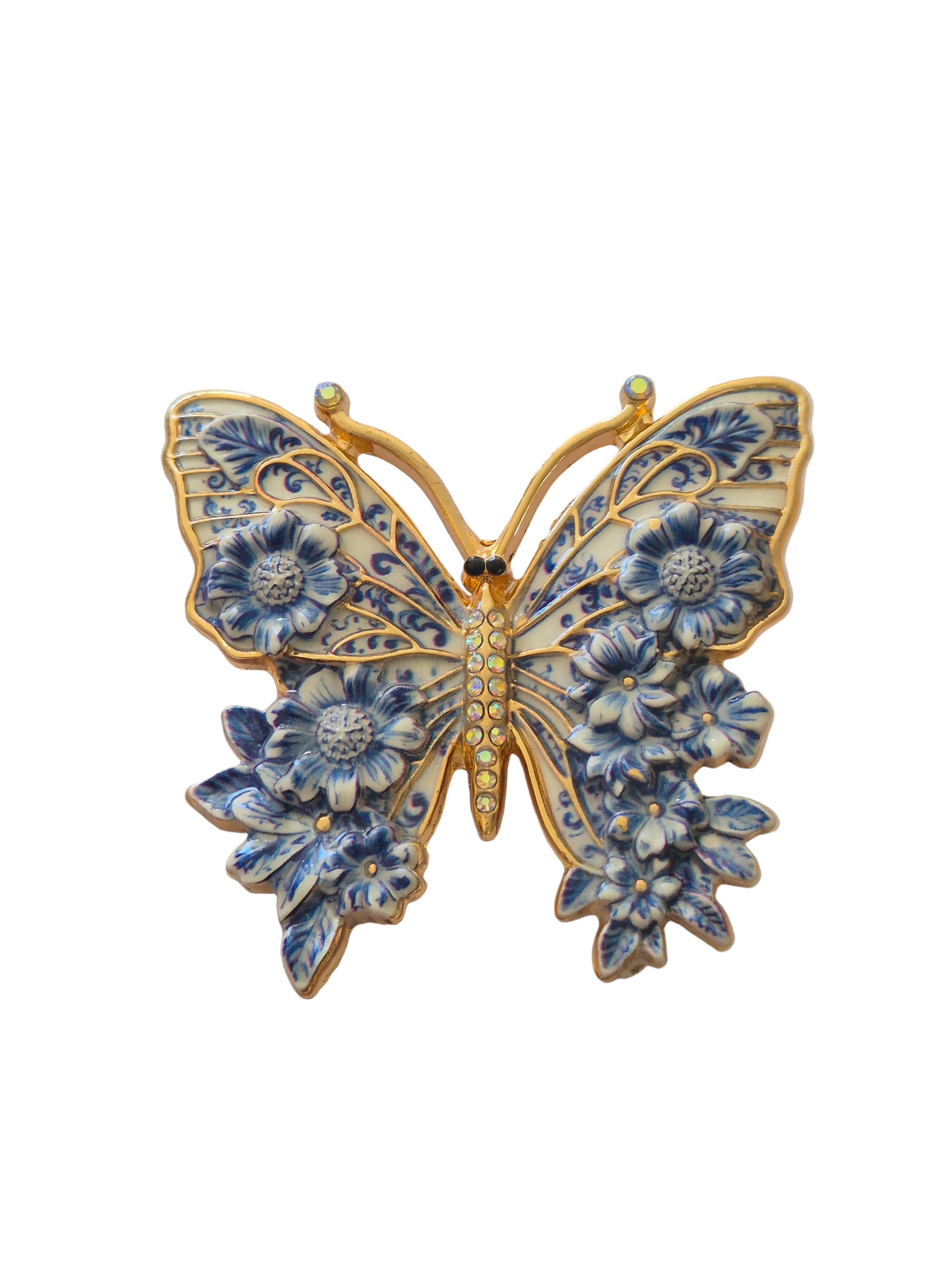 Butterfly-shaped brooch with blue floral patterns and gold accents on a white background