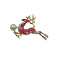 A gold-toned reindeer brooch with red enamel, clear rhinestones, and a white faux-pearl bead, shown on a plain white background.