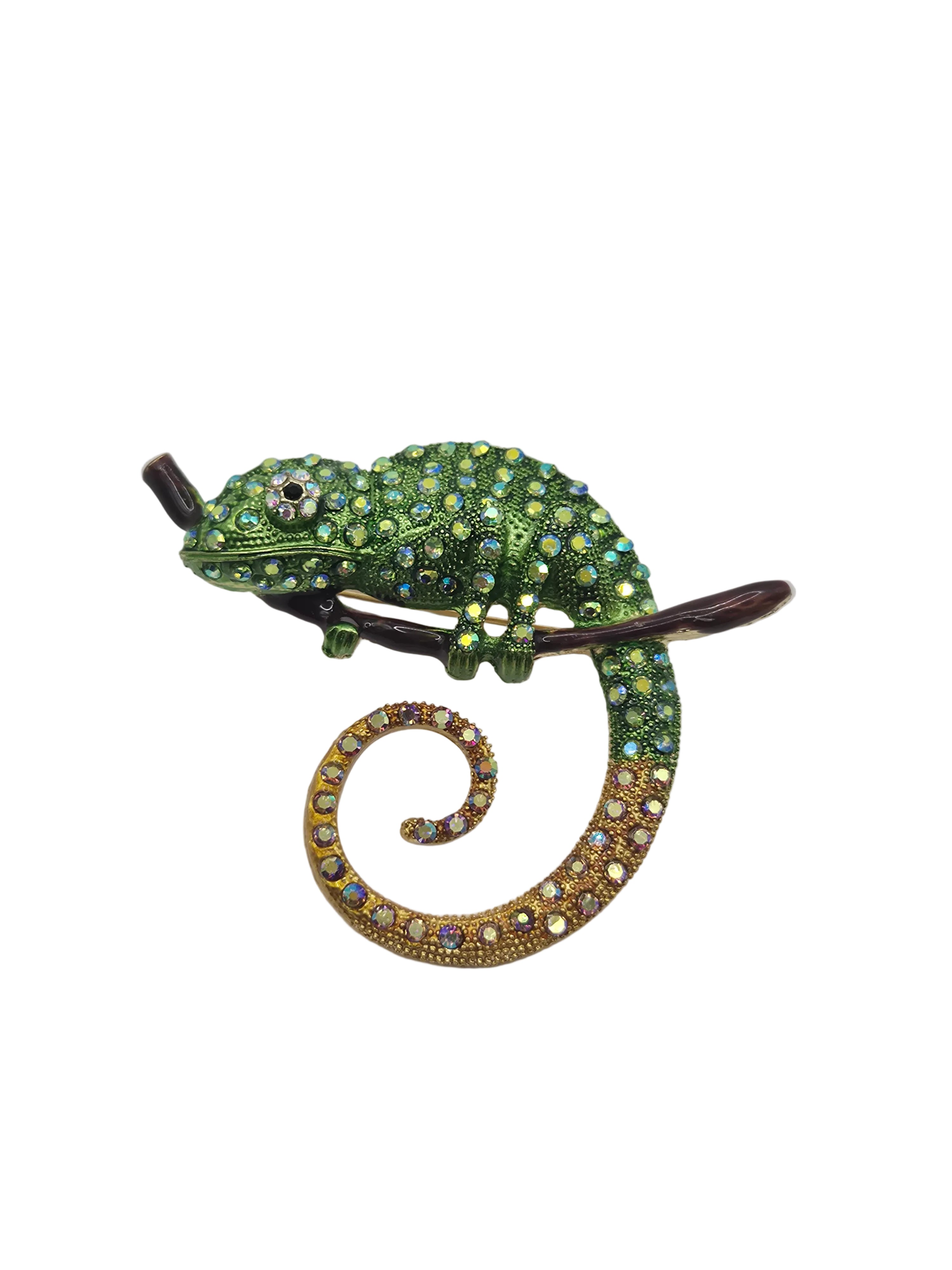 A decorative lizard or chameleon-shaped brooch embellished with green rhinestones and a curled tail paved with gold and iridescent rhinestones, shown on a plain white background.