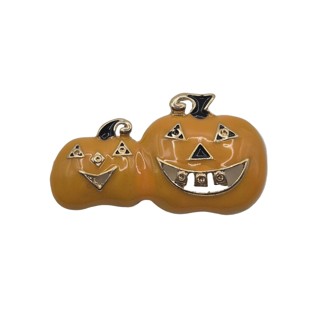 A pair of orange pumpkins with gold-tone metal jack-o'-lantern faces and black enamel details, shown on a plain white background.