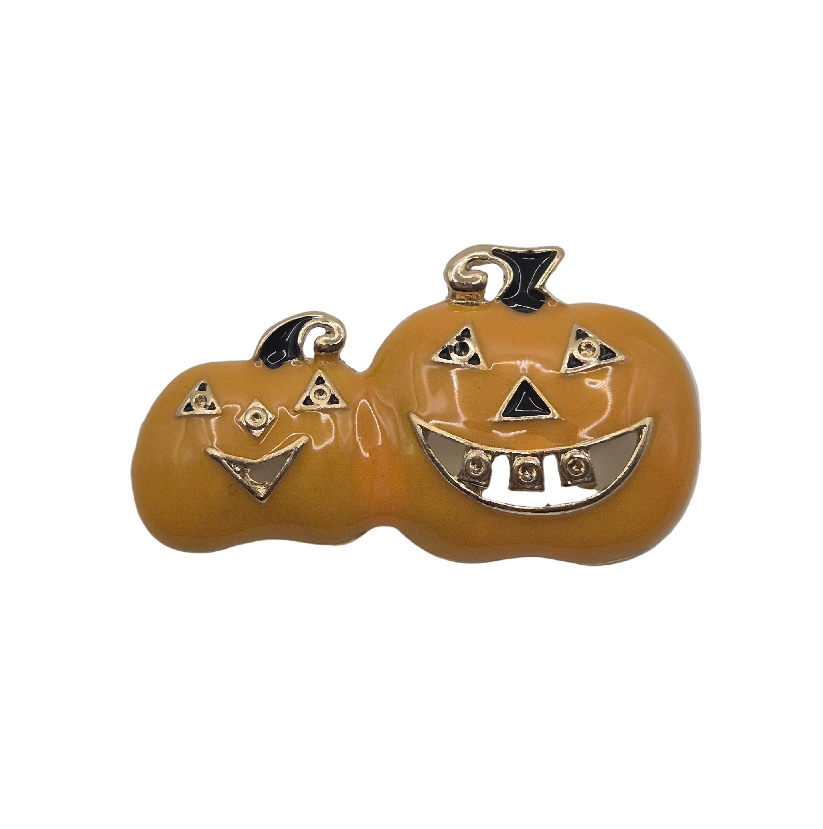 A pair of orange pumpkins with gold-tone metal jack-o'-lantern faces and black enamel details, shown on a plain white background.