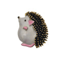 A small hedgehog-shaped brooch pin with a glossy white body, pink ears and feet, and black spines tipped with gold, photographed on a plain white background.