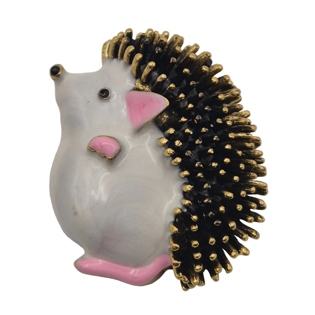 A decorative hedgehog-shaped brooch pin with a glossy white body, black and gold spines, pink ears and feet, and a small gold-tone eye. Shown against a plain white background.