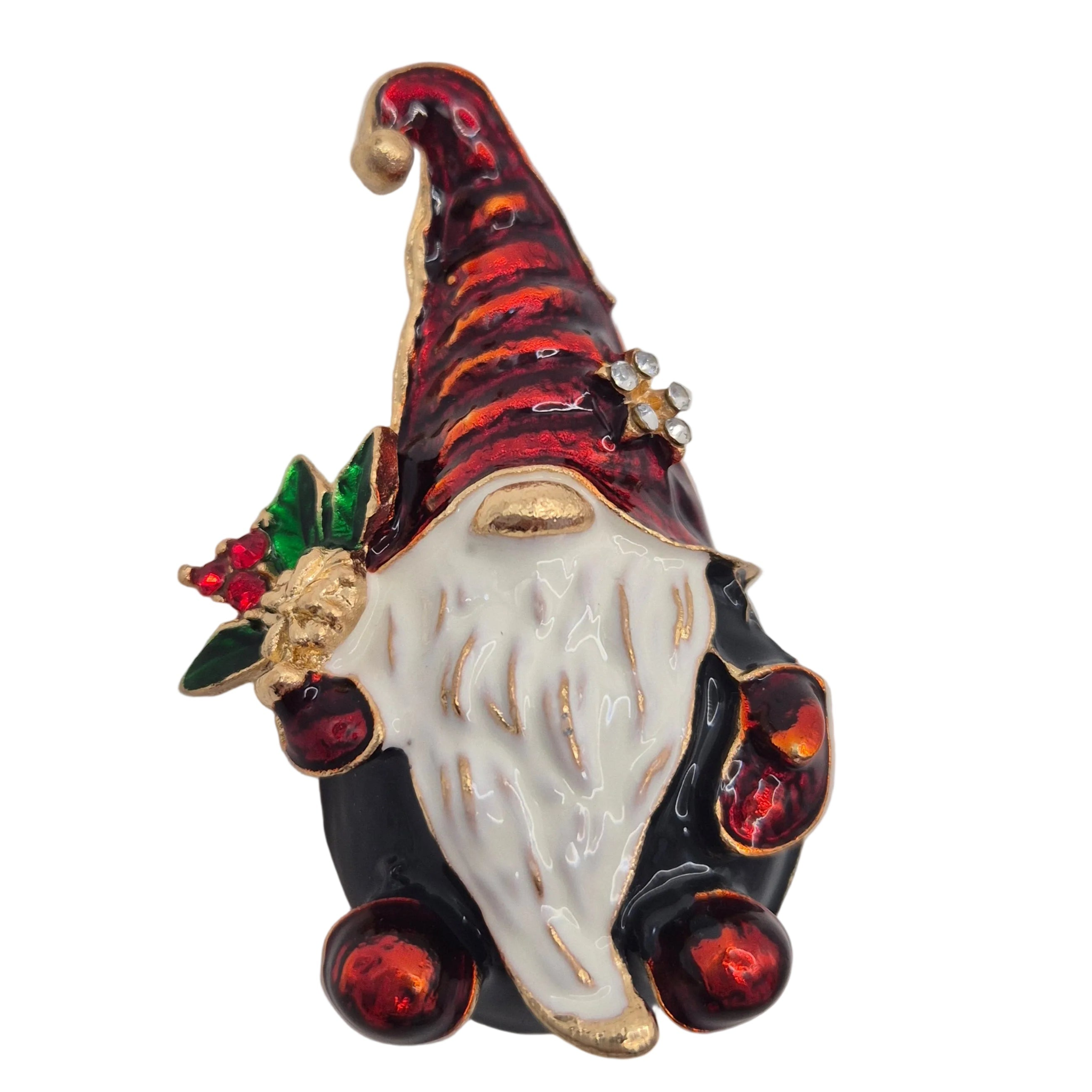A Christmas gnome brooch with a red striped hat, white beard, black body, and red ornaments, accented with gold trim and a small green holly sprig on a plain white background.