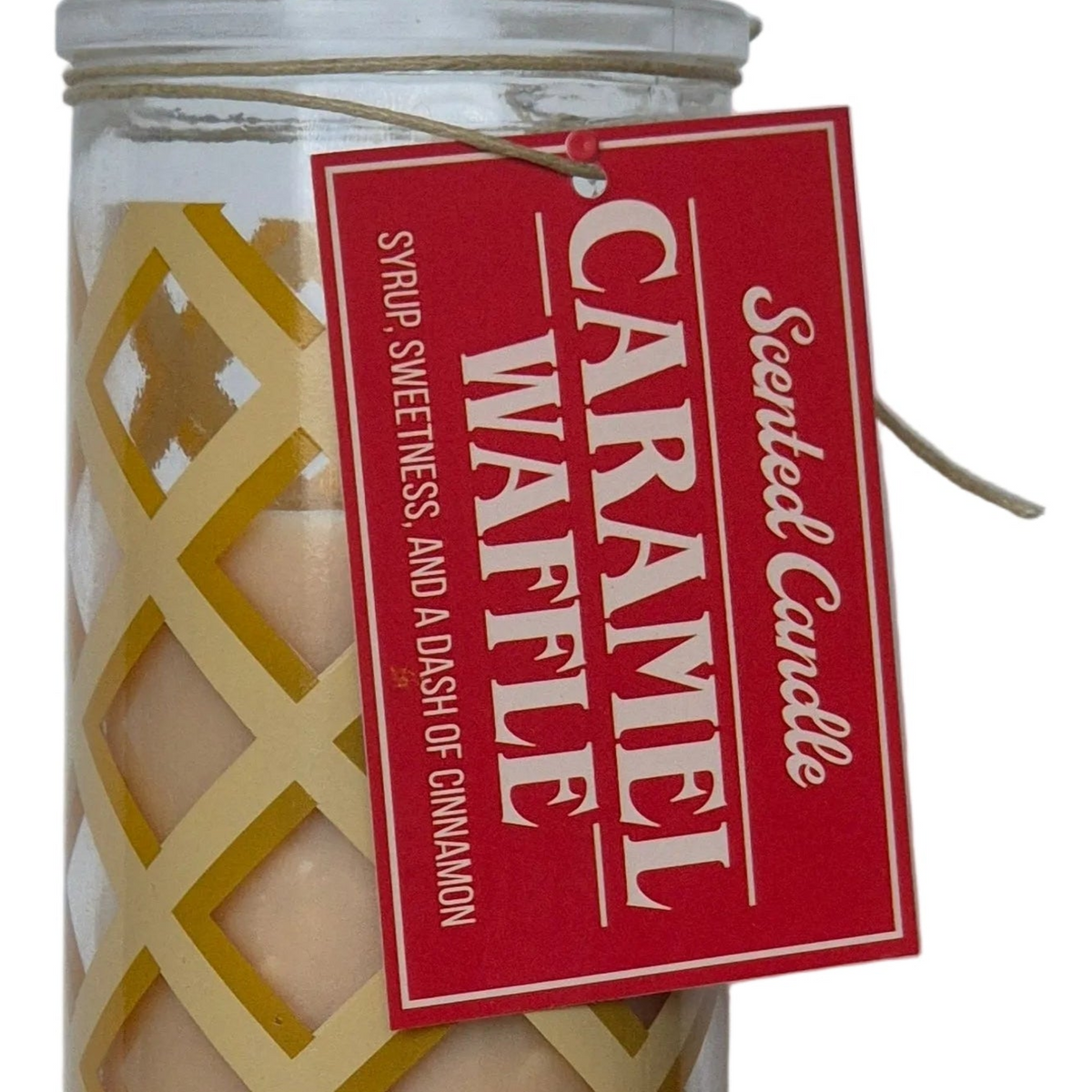A jar candle with a red hanging tag that reads 'Caramel Waffle' and 'Scented Candle.' The candle inside appears pale beige, and the jar has a gold lattice pattern on the front.