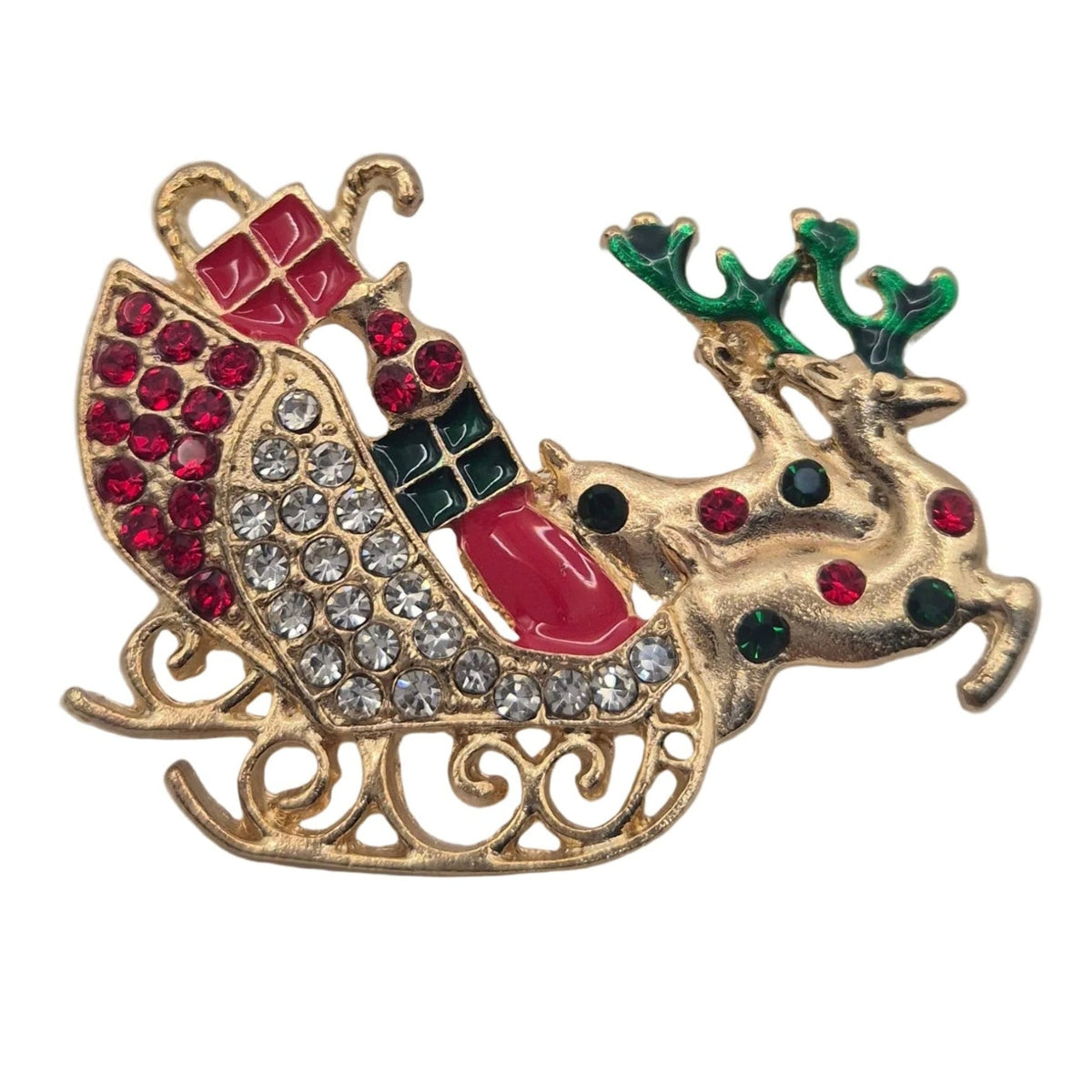A gold Christmas-themed brooch featuring a sleigh filled with red and green gift boxes, decorated with clear rhinestones, and accompanied by a reindeer with green antlers, shown on a plain white background.