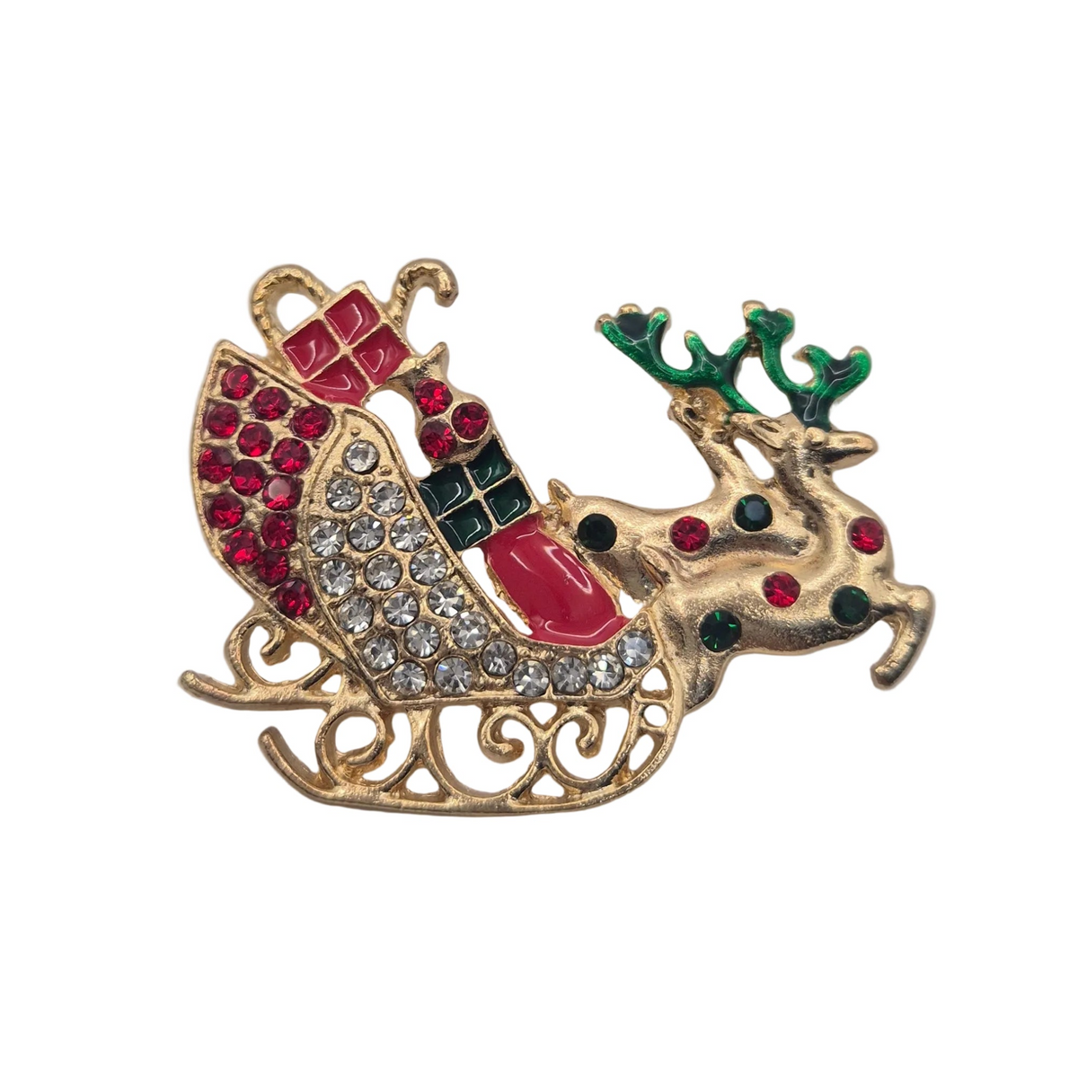 A Christmas-themed brooch featuring a gold-toned sleigh carrying a reindeer, embellished with red and clear rhinestones, green antlers, and red and green enamel details, set against a plain white background.