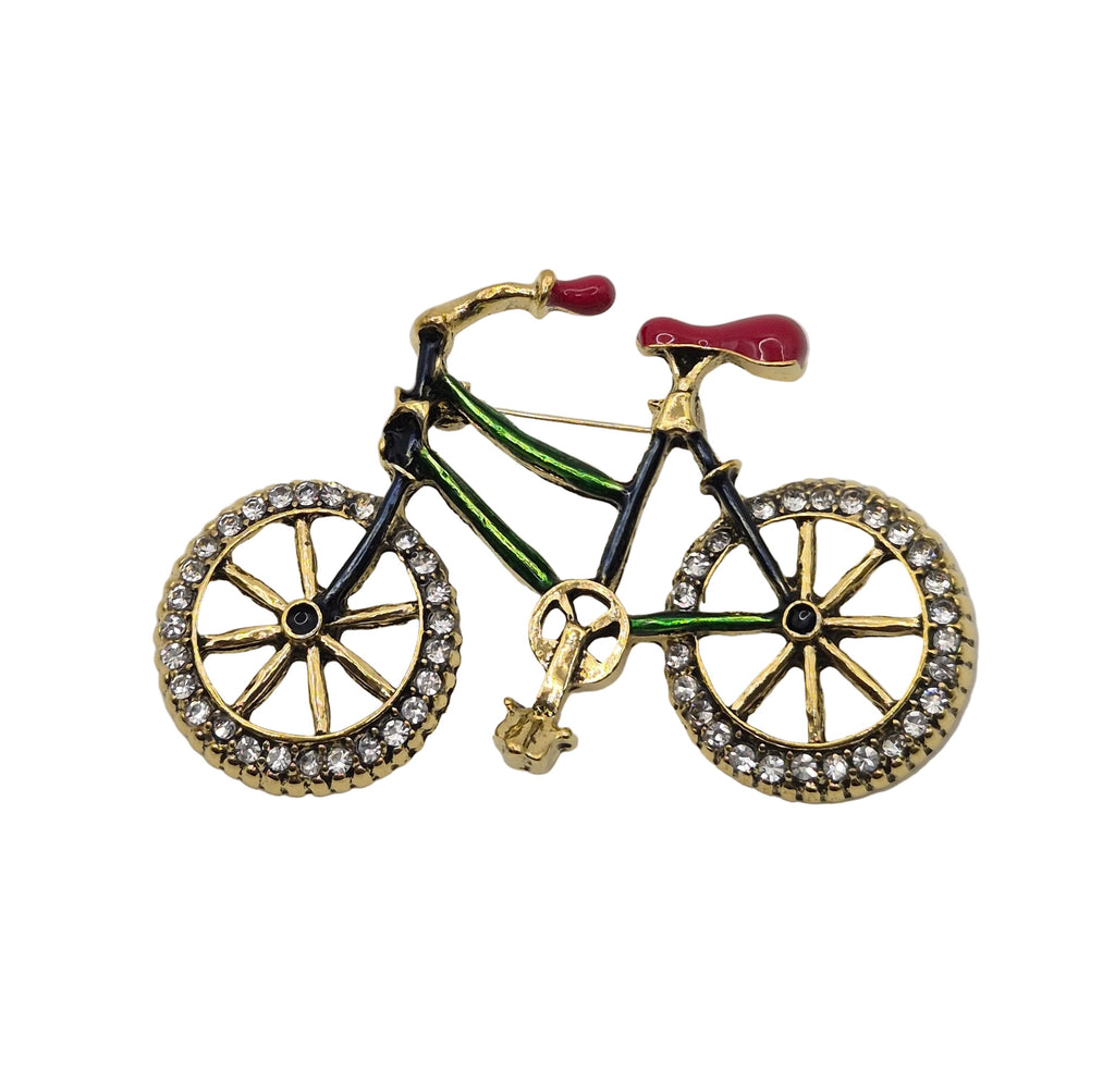A bicycle-shaped brooch featuring gold-tone metal with green, black, red, and clear rhinestone details, set against a plain white background.